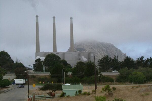 Smokestacks at Morro Bay, California, pictured before the plant shut down in 2014. Behind it is the volcanic plug Morro Rock, which has protected status and faces the beach in front of the stacks. Image: Wikimedia user Robert Ashworth.